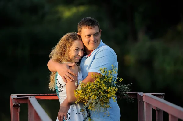 男は日没の夏に手に野生の花の黄色い花束を持つ若い女性を抱きしめます。彼らは目をそらして微笑む。肖像 画。クローズ アップ。画像の水平方向 — ストック写真