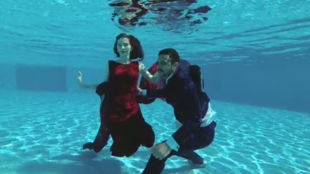 Een paar in de liefde, de bruid en bruidegom, zwemmen onder het water in het zwembad in trouwjurken. Ze glimlachen, genieten en spelen. Slow Motion. Bruiloft onderwater fotograferen. 4k. 25 fps — Stockvideo