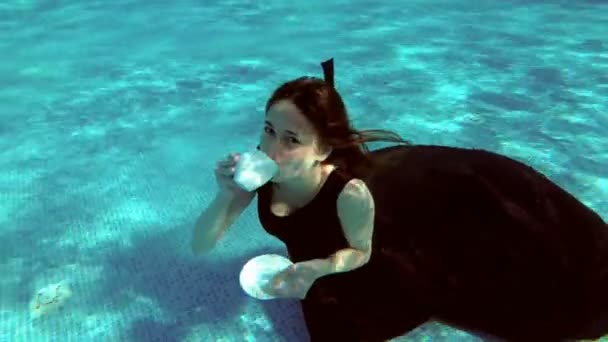 Ragazza carina con un vestito seduto sott'acqua in fondo alla piscina. Beve da una tazza bianca e galleggia in superficie, sorridendo e guardando la macchina fotografica. Al rallentatore. Lavorazione vintage. 4K — Video Stock