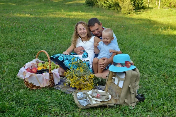 Bonne famille reposant dans le parc sur l'herbe au coucher du soleil. Ils jouent et sourient. Pique-nique en famille à l'extérieur. Portrait. Vue horizontale — Photo