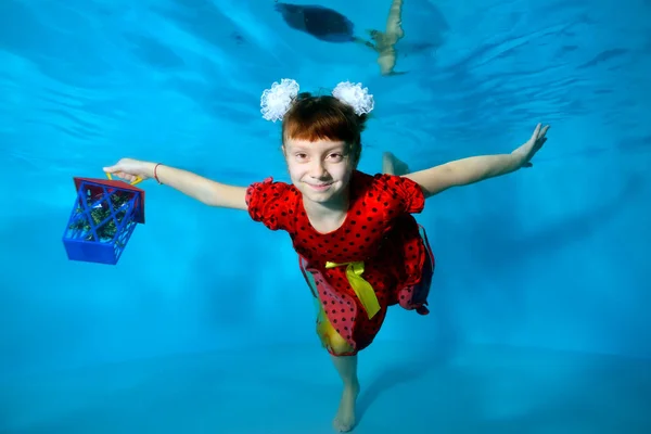 Elinde hediye olan mutlu küçük kız, gözleri açık ve havuzda su altında yüzüyor ve gülümsüyor. Portre. Yatay görünüm — Stok fotoğraf