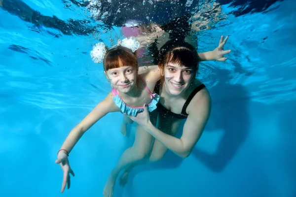 Mutlu anne ve küçük kızı spor yapmak ve gözleri açık havuzda sualtı yüzmek. Mavi bir arka plan üzerinde su altında sarılıp gülümserler. Portre. Yatay görünüm — Stok fotoğraf