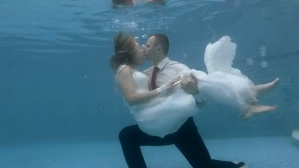 Newlyweds in wedding dresses kissing underwater in the pool and blow bubbles. Wedding underwater. Portrait. Zoom. 4K. 29,97 fps — Stock Video