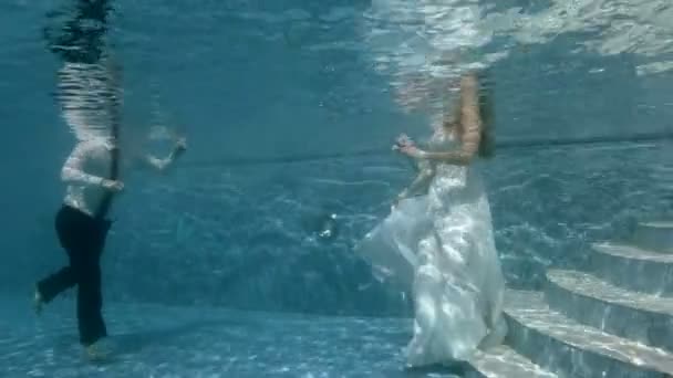 An einem sonnigen Tag tauchen Braut und Bräutigam in weißen Brautkleidern auf den Grund des Pools. Hochzeit unter Wasser. Porträt. 4k. 29,97 fps — Stockvideo