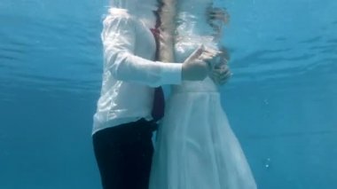 Beyaz elbiseli büyüleyici gelin ve damat, Güneşli günde mavi arka planda havuzda su altında öpüşme ve sarılma. Portre. Yakından kapatın. 4k. 29.97 fps