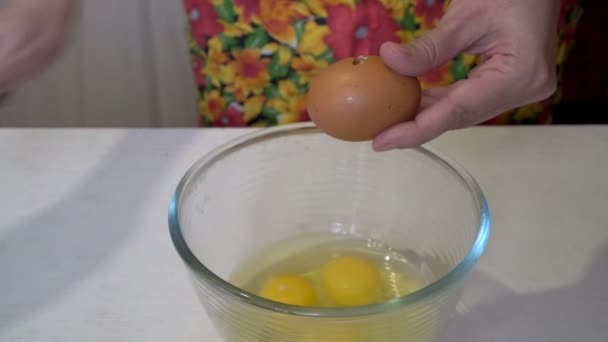 Una mujer rompe huevos de pollo en un recipiente de vidrio en la cocina de la casa para preparar el desayuno. Primer plano. La vista desde arriba. 4K. 25 fps — Vídeo de stock