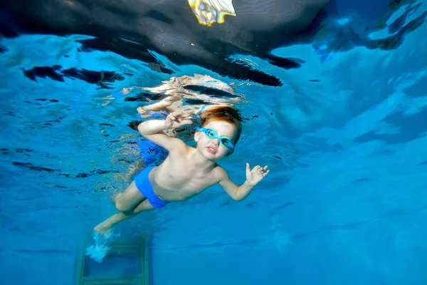 Deportivo niño nada bajo el agua en la piscina cerca de la superficie del agua, mirando y posando para la cámara. Retrato. Fotografía submarina. Orientación horizontal — Foto de Stock