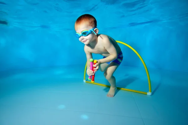 Lindo bebé bucea bajo el agua y tira de los juguetes desde el fondo de la piscina. Retrato. Fotografía submarina. Orientación horizontal — Foto de Stock