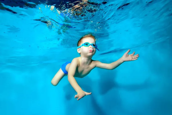 Feliz niño nadando bajo el agua en la piscina y soplando burbujas sobre fondo azul. Retrato. Fotografía submarina. Orientación horizontal — Foto de Stock