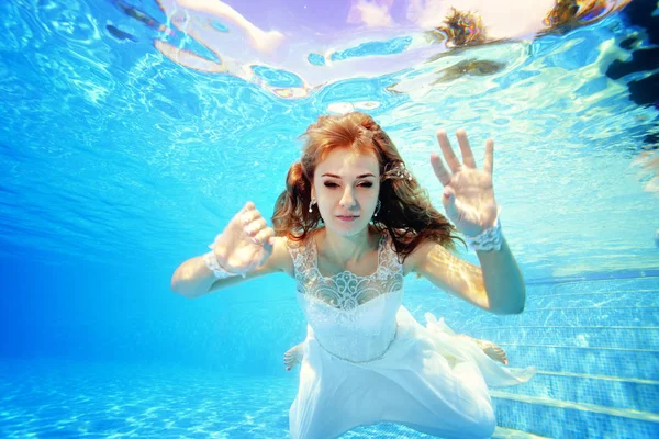 かわいいブロンドの花嫁は白いドレスでプールで水中を泳ぎ、晴れた日にカメラでポーズをとります。肖像 画。クローズアップ。水中で結婚式水中写真。水平方向のビュー — ストック写真