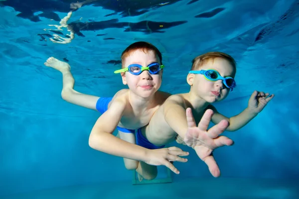 Dos niños felices nadan, se acurrucan y juegan bajo el agua en la piscina sobre un fondo azul. Retrato. De cerca. Fotografía submarina. Orientación horizontal de la imagen — Foto de Stock