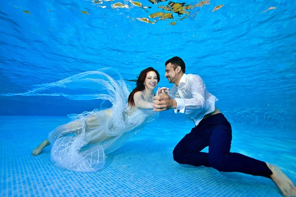 Novia sonriente y novio en trajes de novia nadar y jugar bajo el agua en el fondo de la piscina en un día soleado. Se ríen y posan para la cámara. Retrato. Boda bajo el agua — Foto de Stock