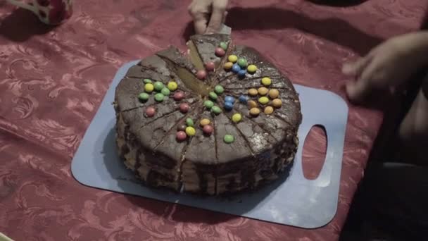 A woman lays out on plates pieces of sliced chocolate cake, decorated with candy on top and treats them to children. Family celebration. Close up. The view from the top. 4K — Stock Video
