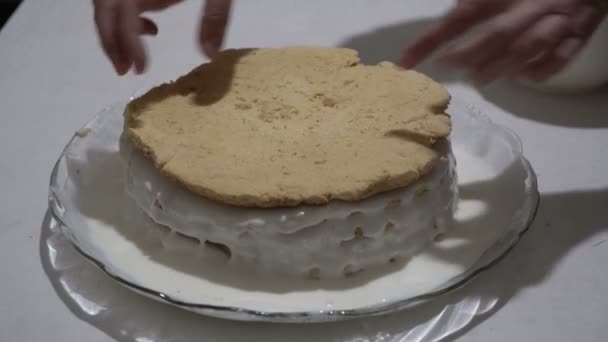 De vrouwelijke chef-kok zet een nieuwe laag op de biscuit taart en smeert het met crème op een glazen plaat. Bereiding van zoete dessert. Close-up. Het uitzicht vanaf de top. 4k — Stockvideo