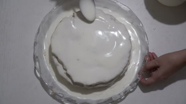 Το κορίτσι ετοιμάζει ένα κέικ και το χύνει με λευκή κρέμα και σοκολάτα. Το πασαλι-χώνεται στην επιφάνεια της τούρτας. Παρασκευή γλυκού επιδόρπιο. Η θέα από πάνω. 4K. — Αρχείο Βίντεο