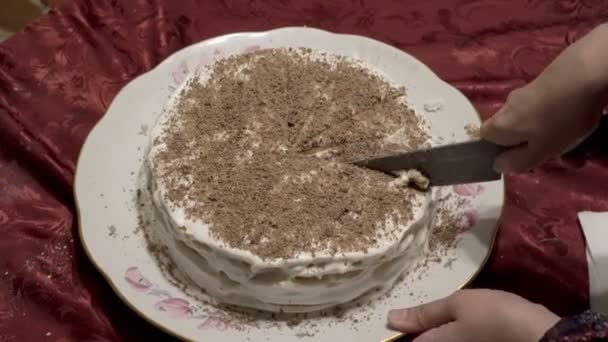 Een vrouw snijdt in gelijke stukken een feestelijke witte taart versierd met geraspte chocolade op de top. Cake is de moeite waard op een wit bord en rode tafelkleden. Close-up. Het uitzicht vanaf de top. 4k — Stockvideo