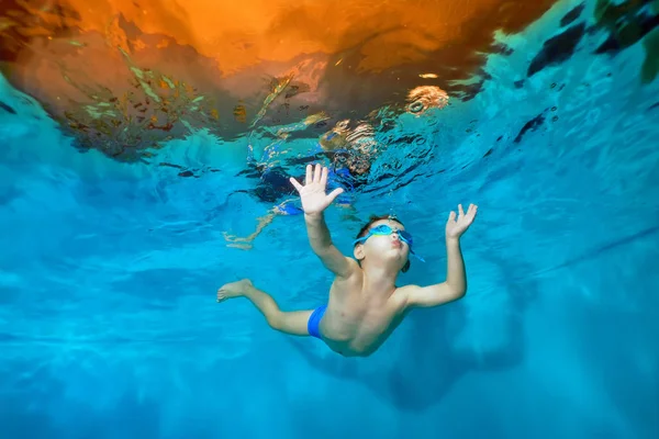 Un niño está flotando bajo el agua en la piscina con los brazos extendidos. Bailando bajo el agua. Creativo. Retrato. Fotografía submarina. Orientación horizontal de la imagen — Foto de Stock