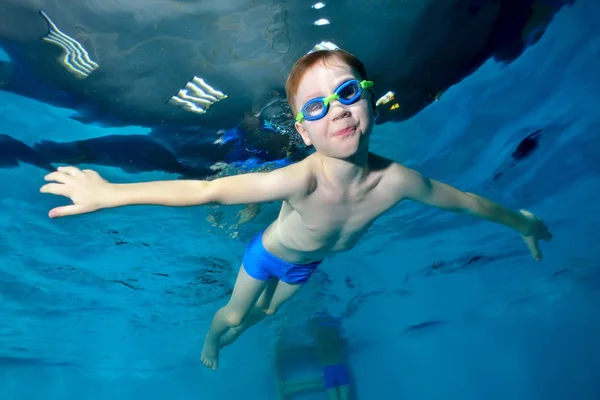 Sonriente chico deportivo nadando bajo el agua, en la superficie del agua. Brazos extendidos como un pájaro. Posando para la cámara con los ojos abiertos. Retrato. Foto bajo el agua. Vista horizontal — Foto de Stock