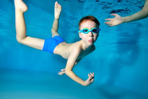 Un niño feliz entra a hacer deporte y nada bajo el agua en la piscina con los brazos extendidos. Retrato. De cerca. Fotografía submarina. Orientación horizontal — Foto de Stock
