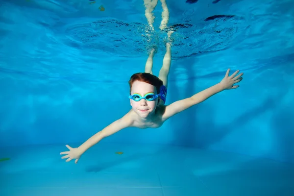 Pequeño chico deportivo sonriendo nada bajo la superficie del agua, extendiendo sus manos a los lados. Posando con los ojos abiertos. Retrato. Fotografía submarina. Orientación horizontal de la imagen — Foto de Stock