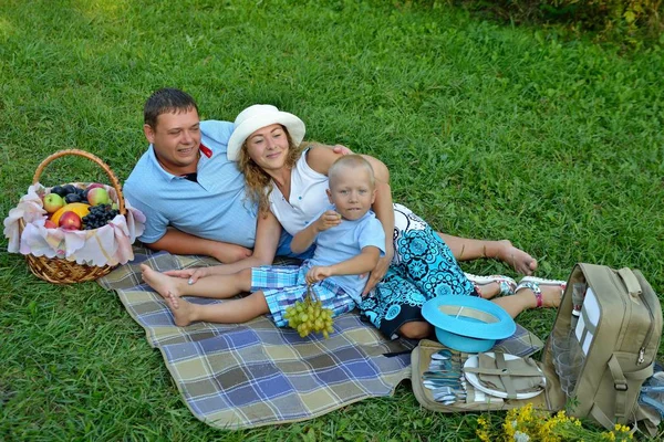 Família feliz: mãe, pai e menino. Piquenique na natureza em um dia de verão. Rapaz a comer uvas. Mamãe de chapéu e papai, sorrindo olha para seu filhinho na natureza. Retrato. Vista horizontal — Fotografia de Stock