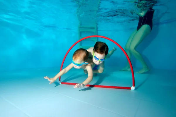 Dos niños deportistas nadan bajo el agua. Rebozar y nadar a través del rojo. Vista desde la parte inferior de la piscina. Retrato. Fotografía submarina. Vista horizontal — Foto de Stock