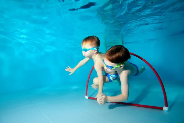 Los chicos deportivos nadan bajo el agua. Jugar y nadar a través del aro rojo. Vista desde la parte inferior de la piscina. Retrato. Fotografía submarina. Vista horizontal — Foto de Stock