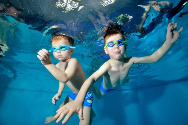 Dos niños felices, hermanos, nadan y juegan bajo el agua en la piscina sobre un fondo azul. Posando para la cámara. Retrato. Fotografía submarina. Orientación horizontal — Foto de Stock