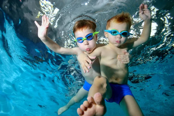 Dos niños sonrientes, hermanos, nadan y juegan bajo el agua en la piscina. Abrazando y posando para la cámara. Retrato. Fotografía submarina. Orientación horizontal — Foto de Stock