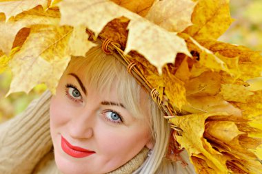 Sarı sonbahar bir çelenk içinde sevimli büyük sarışın sarı bir arka planda ormanda yaprakları, çerçevede bakıyor. Boyut Plus XXL kadın. Portre. Yakın çekim