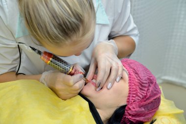 Güzel bir kız-Kozmetolog güzellik salonunda dudakların kalıcı makyaj prosedürü yok. Üstteki görünüm. Kavram. Görüntünün yatay yönü