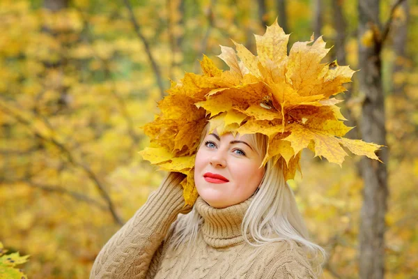 Чарівна блондинка в вінку осіннього листя, в ніжному джемпері в лісі, вдумливо посміхається. Близько. Розмір жінки плюс Xl — стокове фото