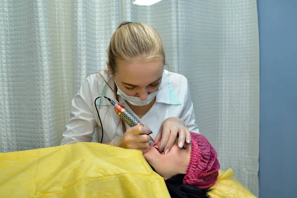 En el salón de belleza, una maestra esteticista, una rubia hace permanentes labios de maquillaje chica europea. Concepto. De cerca. Orientación horizontal de la imagen — Foto de Stock