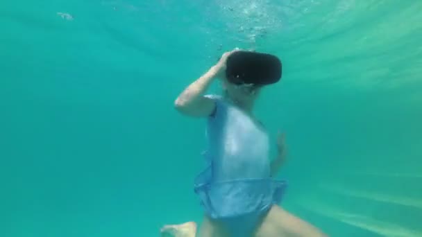 A young girl playing virtual games under water. She dives to the bottom of the pool in a virtual reality helmet and waves her hands. The concept of immersion in a virtual environment. Close up. 4K — Stock Video