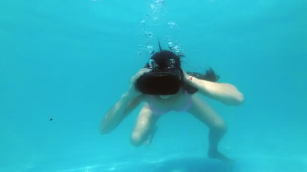 Спортивная взрослая девушка ныряет в воду в черных очках виртуальной реальности. Она плавает в бассейне и играет в виртуальные игры в необычной обстановке. Концепция виртуальной среды. Медленное движение. 4K — стоковое видео