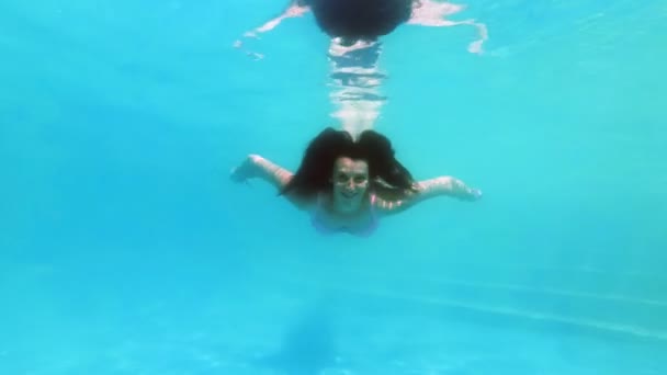 Une jolie fille va faire du sport dans la piscine et nage sous l'eau à la caméra les yeux ouverts. Elle regarde la caméra, sourit et agite les mains. Ferme là. Au ralenti. 4K . — Video