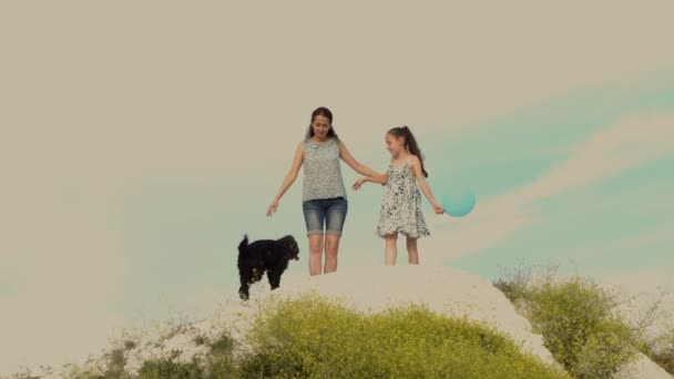 Jeune maman, petite fille et chien sur fond de coucher de soleil au sommet de la colline. Ils rient et s'amusent à jouer avec le chien. Une fille avec une balle dans la main. 4K . — Video