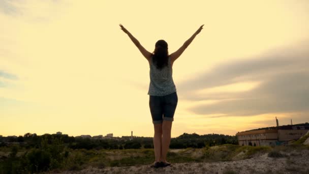 A young graceful girl stands on a hilltop on a Sunny day against a bright sky. She's waving like a bird. 4K. — Stock Video