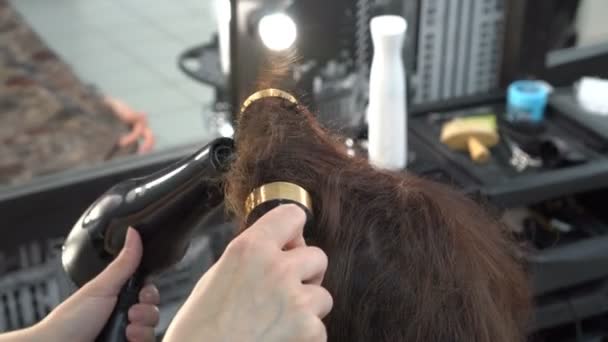 Cabeleireiro estilista seca secador de cabelo e puxa o cabelo com uma escova redonda menina-cliente. Close-up. 4K . — Vídeo de Stock
