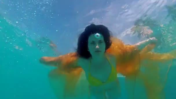 Dalgalı kumaşlar ve uzun saçlı, su altında poz veren sarı mayolu güzel genç kız. Yüzüyor, kollarını dışarı çıkarıyor ve kameraya bakıyor. 4k — Stok video