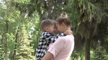 Mutlu bir genç anne kollarında neşeli, gülen bir bebek tutar. Onlar sarılmak ve şehir Park yeşil ağaçların arka plan karşı kafa kafaya sarılmak. Küçük bir çocuk şaka yapıyor ve kameramanı korkutuyor. 4k