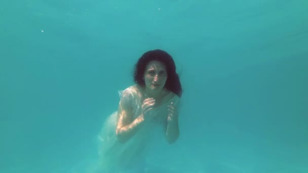 Retrato de moda. La novia en un vestido blanco nada y posa para la cámara bajo el agua en la piscina en un día de verano. Concepto. En cámara lenta. Primer plano. 4K . — Vídeos de Stock