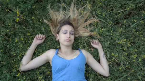 一个可爱的年轻金发女孩在自然的肖像。她躺在被黄色野花包围的草地上，抬头一看，做梦。特写。顶部的视图。4k. — 图库视频影像
