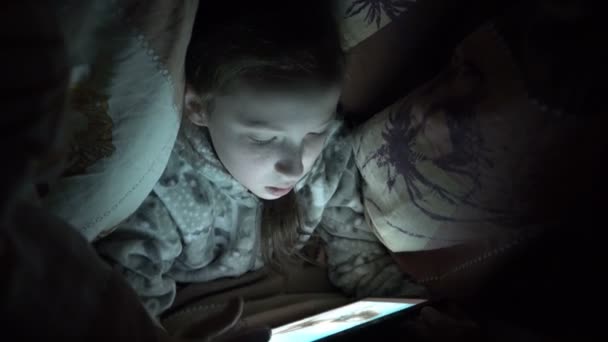 Cute Little Girl w nocy w ciemności grając na tablecie pod kocem na łóżku. Film koncepcyjny. Zbliżenie. RAW wideo. 4K. — Wideo stockowe