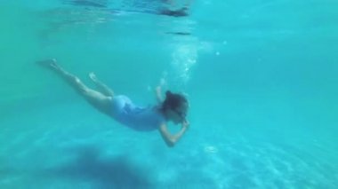 Sportif küçük kız dalış ve güneşli bir günde açık havuzda sualtı yüzer. Dibine yakın yüzüyor ve kameraya bakıyor. Yavaş çekim. Close. 4k.