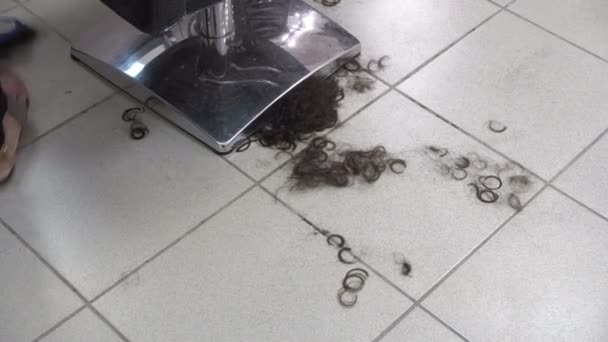 Una limpiadora barre el cabello en el suelo con una escoba en una peluquería después de cortar a un cliente. Trabajo en una peluquería. La vista desde arriba. Primer plano. 4K . — Vídeos de Stock