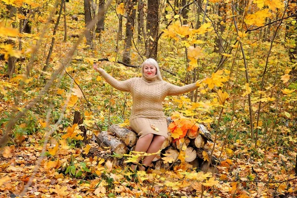 A pretty middle-aged woman throws up autumn leaves on a Sunny day in the forest. Looking at the frame and smiles. Women\'s plus size xxl. Horizontal view.