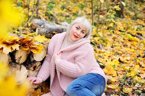 Une belle blonde d'âge moyen pose lors d'une journée ensoleillée d'automne dans la forêt avec un doux pull tricoté.Elle flirte avec du rouge à lèvres écarlate. Taille femme plus xxl. Vue horizontale — Photo