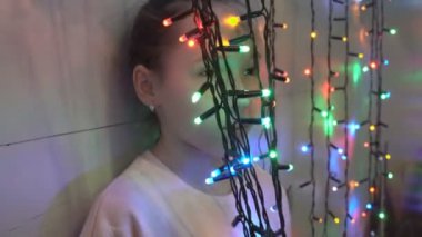 Sevimli bir küçük kız oynuyor ve yanıp sönen çok renkli çelenk bakarak. Şenlikli Noel aydınlatmaları. Tatil aksesuarları. Portre. Close. 4k.