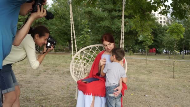 Fotografi professionisti, un uomo e una donna, scattano foto di madre e bambino nel parco su un'altalena. Servizio fotografico di famiglia all'aperto. La vista dall'esterno. Primo piano. 4K . — Video Stock